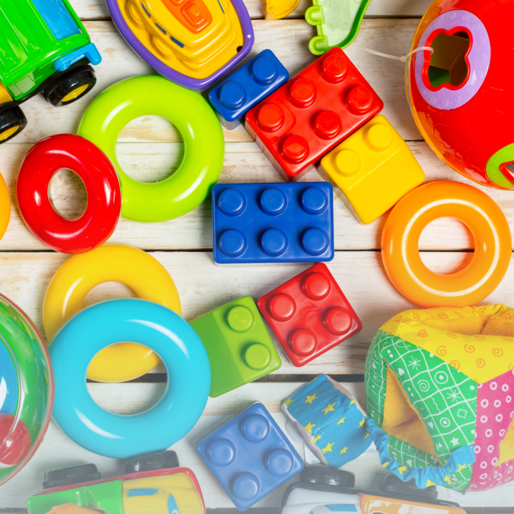 Colorful toys including green and blue rings, red and blue lego blocks and toy cars spread out on a wood floor.