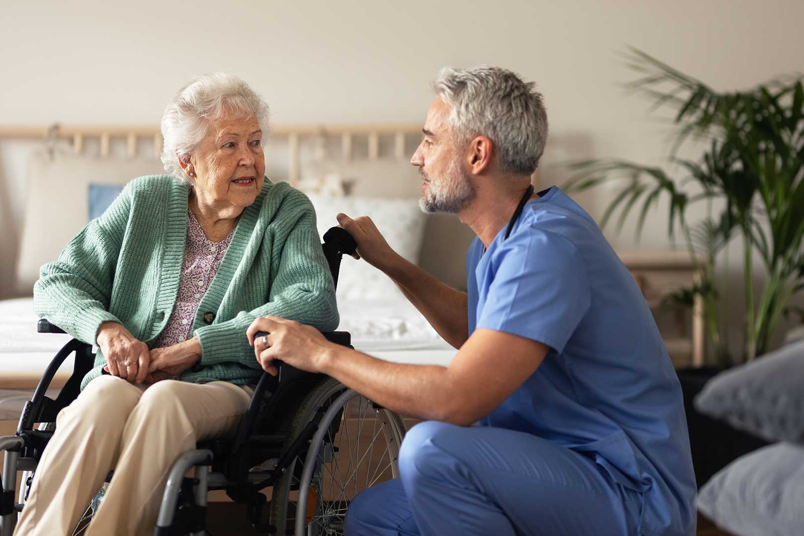 Male caregiver supporting older woman sitting in wheelchair