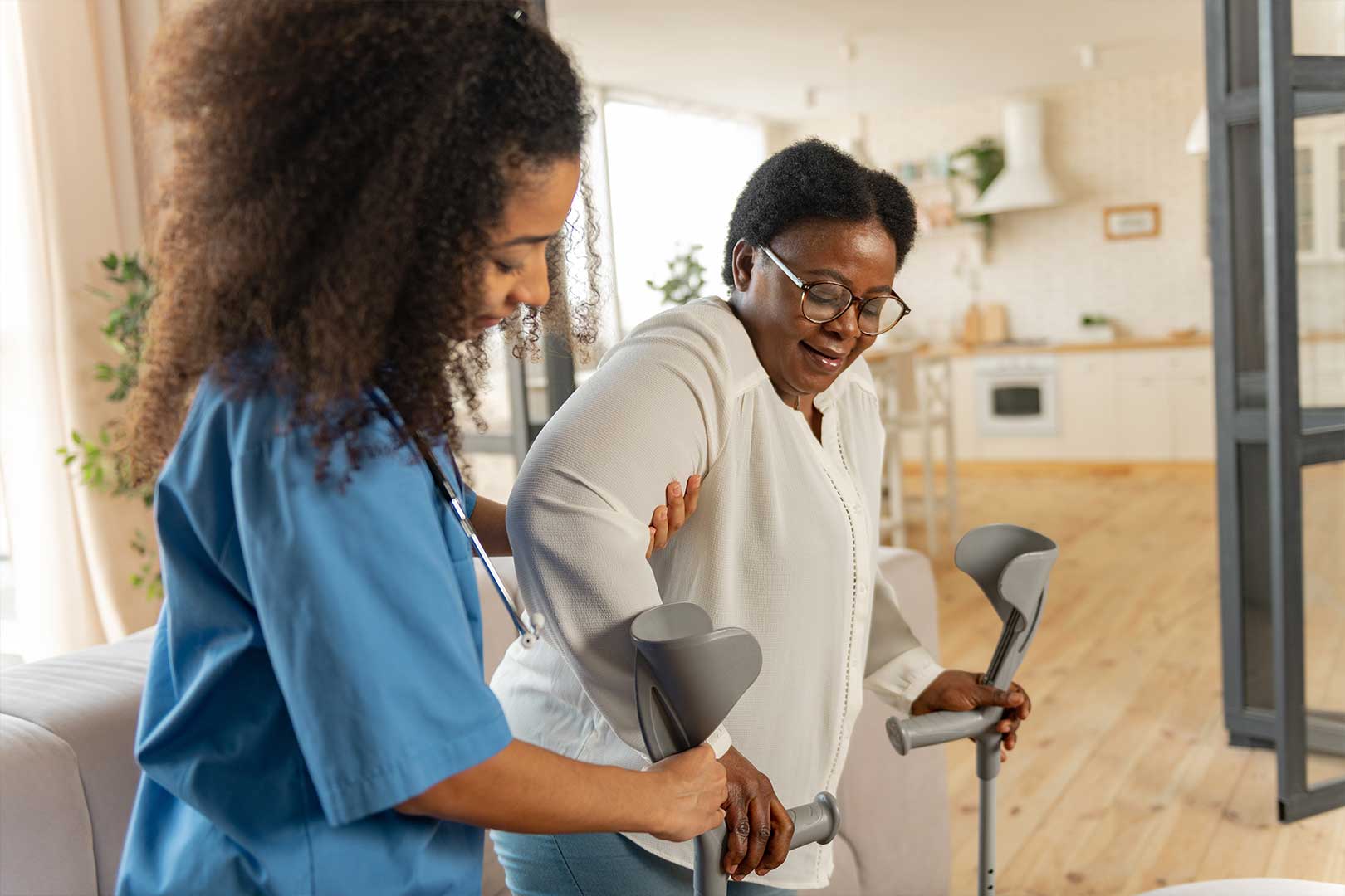 Female caregiver supporting older woman using crutches