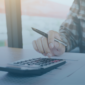 Close up of a white male's hand typing into a calculator. He is also holding a pen in his hand and the sleeve of his shirt is checkered.